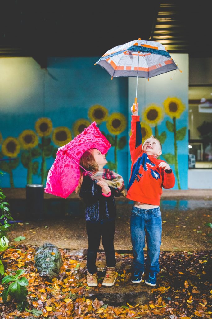 brother and sister play with umbrellas during rainy family photographs in fayetteville arkansas