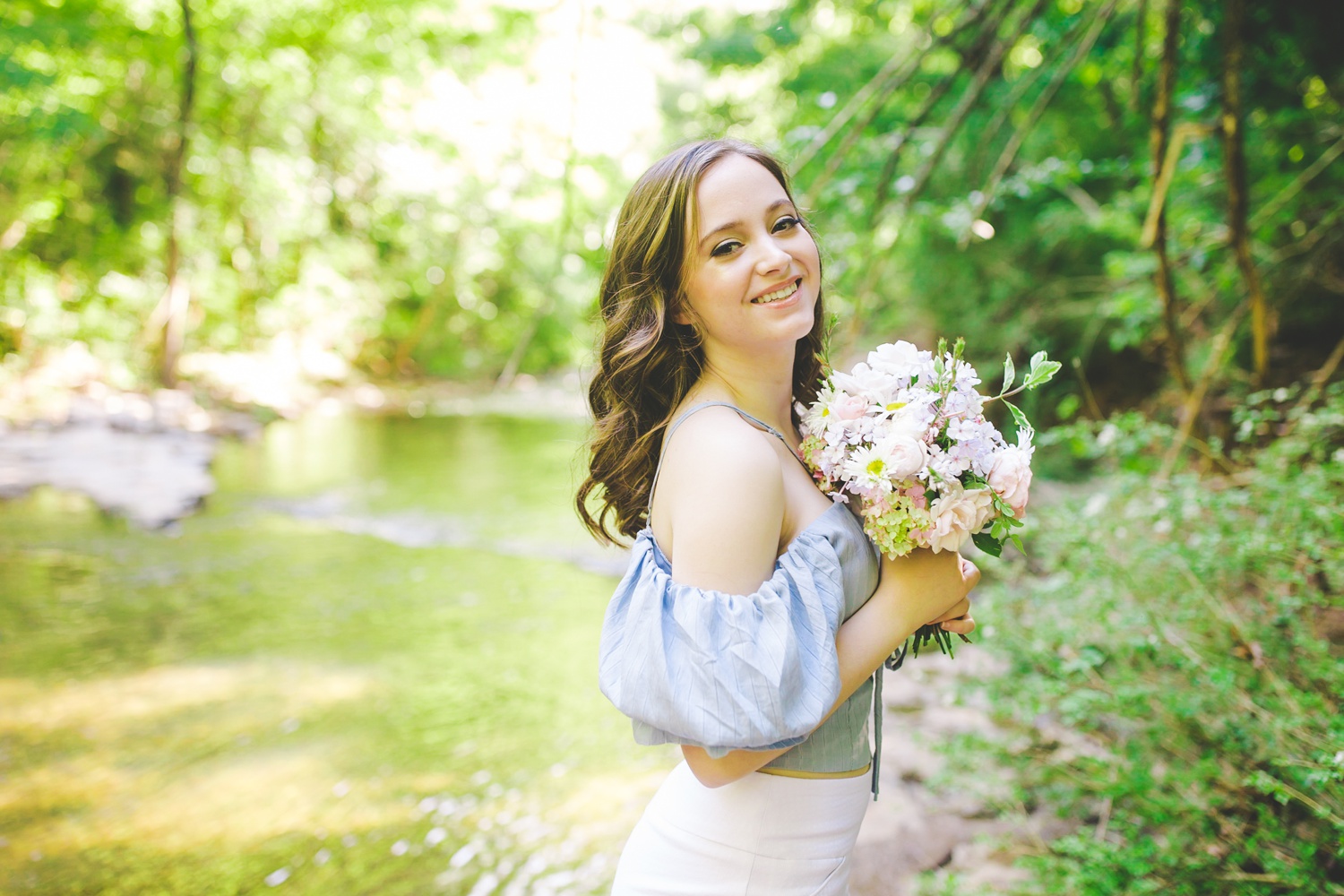 senior photographs at the creek with senior holding flowers